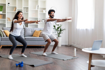 Active indian couple practicing sports at home, making squats together