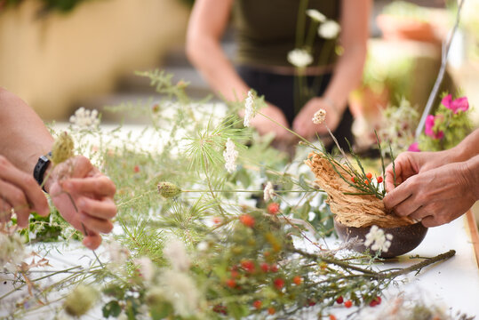 Detail of hands making flower arrangement, outdoor ikebana workshop, different flower arrangements in progress.