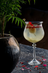 cocktail in a glass on a stem decorated with a red flower and with an olive on a skewer
