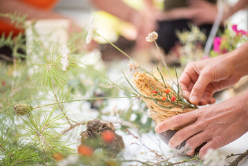 Detail of hands making flower arrangement, outdoor ikebana workshop, different flower arrangements in progress.