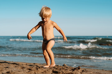 Fototapeta na wymiar little boy 3 years old plays in the sand on the beach near the sea