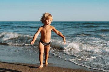 little blond boy 3 years old walks on the water by the sea