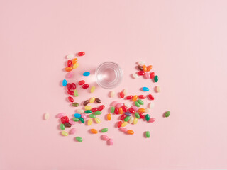 View from above glass of water and jelly beans as colored pills scattered on pink background. Concept of vitamins and food supplement.