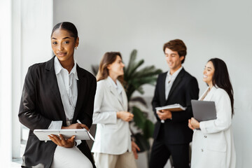 Attractive african american female director CEO sitting at the office table with group of colleagues on the background