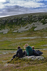 Fototapeta premium Single mother sitting with her children on a rock enjoying the mountain cliff view in tundra landscape of Sweden. Healthy lifestyle family in nature travel tourism concept