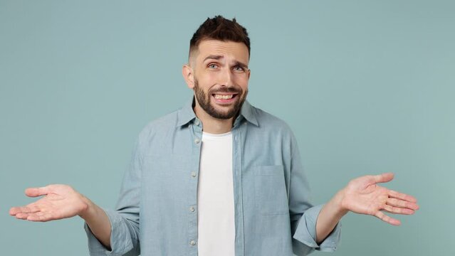 Hesitant indecisive fun shy young man wears shirt white t-shirt feels doubtful spreading hands say oops ouch oh omg i am so sorry isolated on plain pastel light blue cyan background studio portrait