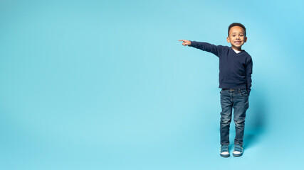 Little black boy pointing aside at free space on blue studio background, demonstrating free place for design or offer