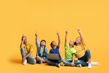 Cute multiethnic children with laptop computer pointing at copy space