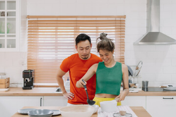 Husband looking at wife who cooking lunch for him. Happy asian couple in kitchen