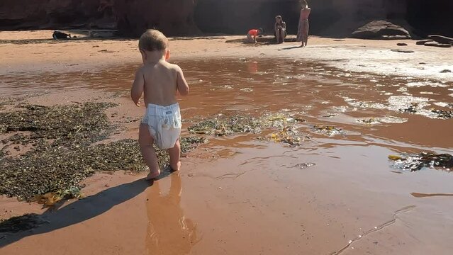 Toddler girl wearing diaper that is big and saggy on beach on bright summer day - cute beach fun