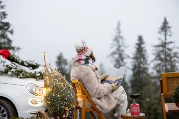 Badkamer foto achterwand Young woman relaxes and enjoys calm on nature during winter holidays, has a picnic and reads some magazine while sitting near lighted Christmas tree in mountains © rh2010