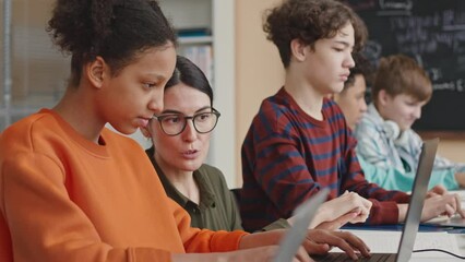 Young Caucasian female teacher helping African American schoolgirl during coding and programming lesson in modern computer class - Powered by Adobe