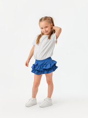A 5-year-old girl in a white T-shirt and blue skirt smiles, hand behind her head. It stands on a...