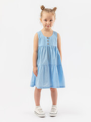 A 5-year-old girl with club-footed legs. She looks at the camera in a blue sundress and sneakers on a white background with an expressive look. Photo.
