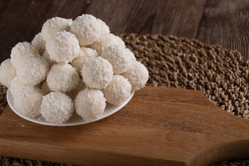 photo of sweet coconut balls lying on a plate and a wooden board.