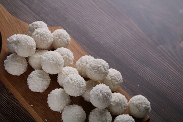 photo round white chocolate candies sprinkled with coconut shavings, dessert sweet food, sugar, on a wooden board