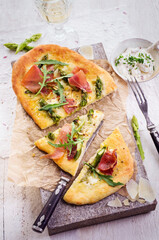 Traditional tarte flambee with green asparagus, prosciutto ham and cheese served as top view on a...