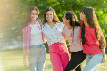 Team of happy smiling women with pink ribbon on t shirts embracing while standing on the street