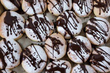 Freshly baked homemade chocolate doughnuts with powdered sugar and melted chocolate on a baking tray. Top table view.