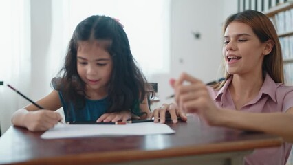 Young teacher woman helping little girl student writing and finish lesson. Happy Asian kid girl giving high five to woman teacher at classroom. Teacher support student and giving high five together