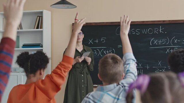 Multiethnic preteen students raising their hands to solve Math equation at blackboard during lesson