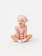 Surprise, a little girl 2 years old in a pink dress and a scarf sits on the floor and looks carefully with her mouth open.