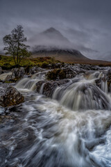 Glencoe, Scotland in the Scottish highlands. Waterfall on a stormy and cloudy day.  Scottish weather, mountains, waterfalls and clouds. 