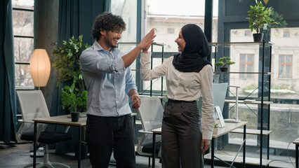 Two multiracial colleagues happy company coworkers Arabian Indian man businessman giving high five muslim woman businesswoman in hijab business people smiling together teamwork partnership in office