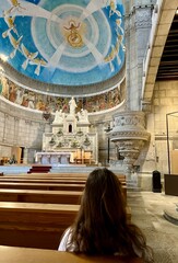 a girl with long hair in a dress sits inside the church and looks at the iconostasis Diocesan...