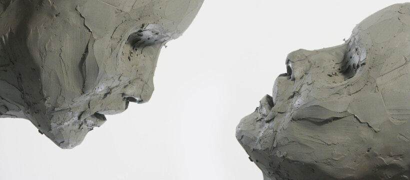 Two clay faces on a white background. Portrait, sketch without eyes. Artwork in process of creation. Banner  of modelling and sculpture, fine arts, figurative and contemporary art.
