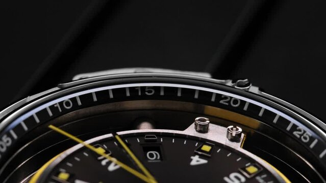 Extreme closeup of yellow second arrow passing by on black clock face. Lengthwise view of luxury swiss watch. Closeup real time shot. Running second arrow. blank dial
