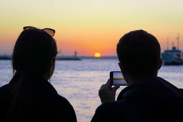 Mobile phone Photography. Two silhouetted people taking a sunset photo. Amateur photography.