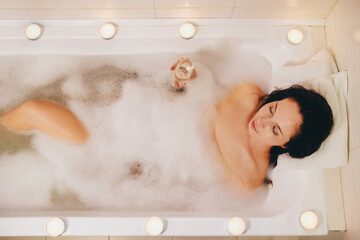 Girl with a glass of white wine in a bubble bath. View from above.