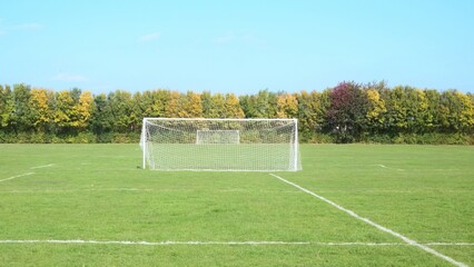 Football soccer goal posts with net on green grass with markings on a beautiful sunny day, trees in background
