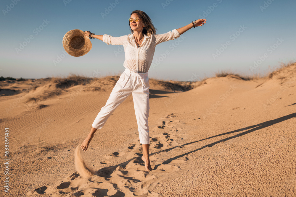 Wall mural stylish beautiful carefree happy woman walking in desert sand dressed in white outfit