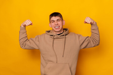 Portrait of young cheerful man over yellow background with fists up.