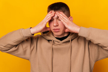 Photo of young man standing over yellow background and having some headache.