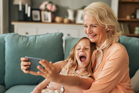 Happy grandmother and granddaughter taking selfie using smartphone in the living room