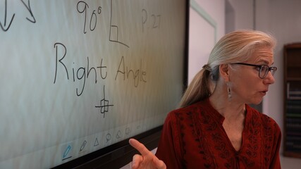 Closeup of happy female teacher writing on an interactive whiteboard teaching geometry math in a school classroom.