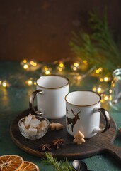 Two empty white mugs on a wooden board on a green concrete background in a Christmas composition. Prepared serving for hot drinks.