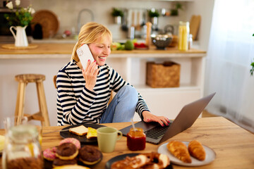 Young woman with laptop talking on the phone at the dining table