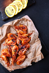 Grilled shrimp on paper. Shrimp with lemon and spices on vintage dark background. Appetizer for beer.Flat lay. Top view.