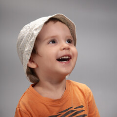 Emotional studio portrait of a cheerful, vibrant boy wearing a Panama hat on a gray background.