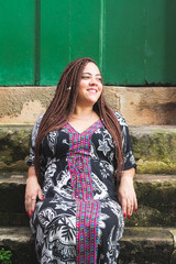 A woman wearing African clothing sits on a cement staircase. Quiet and happy person.