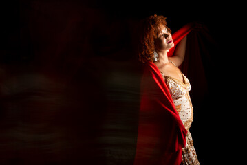 Photo taken at low speed of a beautiful woman with curly red hair with a red cloth over her body