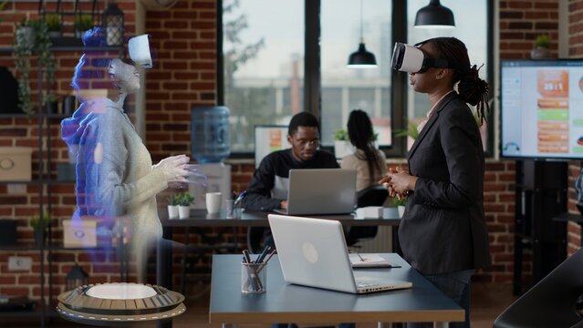 Employee wearing VR goggles with hologram supervisor. Businesswoman at high tech office desk computer watching virtual reality training video visualization of team leader explaining how to solve tasks