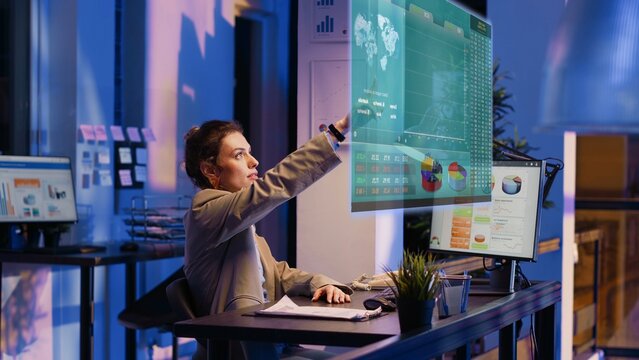 Accountant imputing revenue figures on computer in office during nightshift, visualizing them using augmented reality. Employee at desk focused on typing company statistical numbers, working overnight - Powered by Adobe