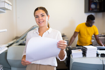 Focused young woman in white shirt checking the print quality and accepting color proofs in typography