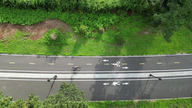 man riding a bicycle on paved bike lane in public park shot (next to pedestrian walkway) asphalt, pavement (drone footage filmed from above) gravel, mountain, road cycling, biking, riding urban