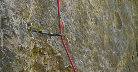 CLOSE UP, DOF: Bolt hanger with attached quickdraw and running climbing rope